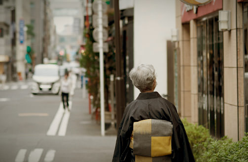 A woman in a kimono walking down an alley around Kotto Dori. It symbolizes the cultural streetscape of Kyobashi, lined with antique stores and galleries.