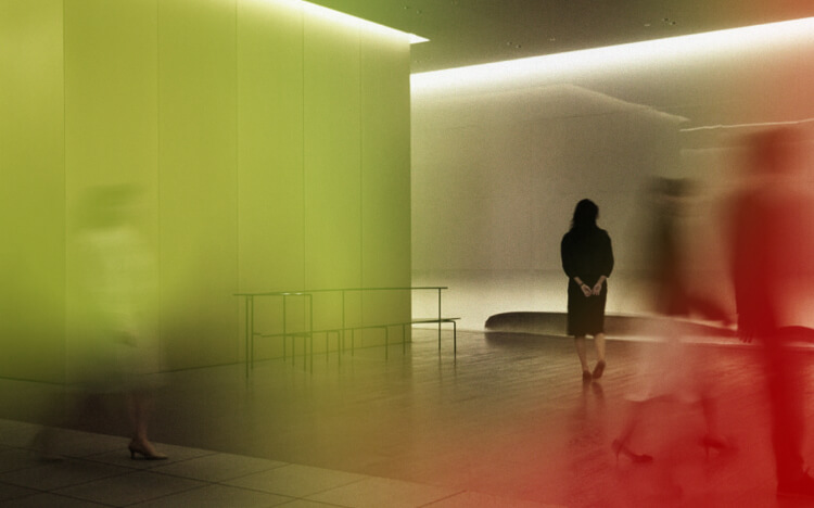 This photograph captures the interior of Museum Tower Kyobashi in a gradient of light. The contrast of stillness and motion is created by the figures standing and the movement of people passing by.