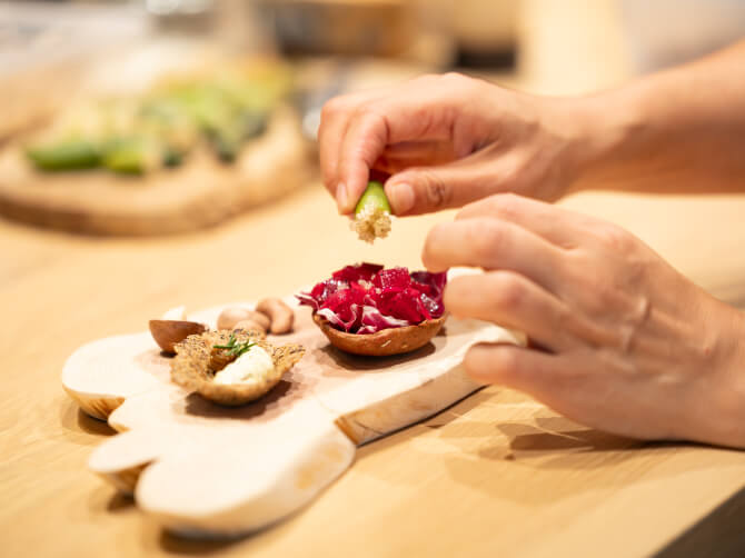 木製のトレイに盛り付けられた前菜に、参加者がフィンガーライムなどの食材を添えて仕上げている様子。