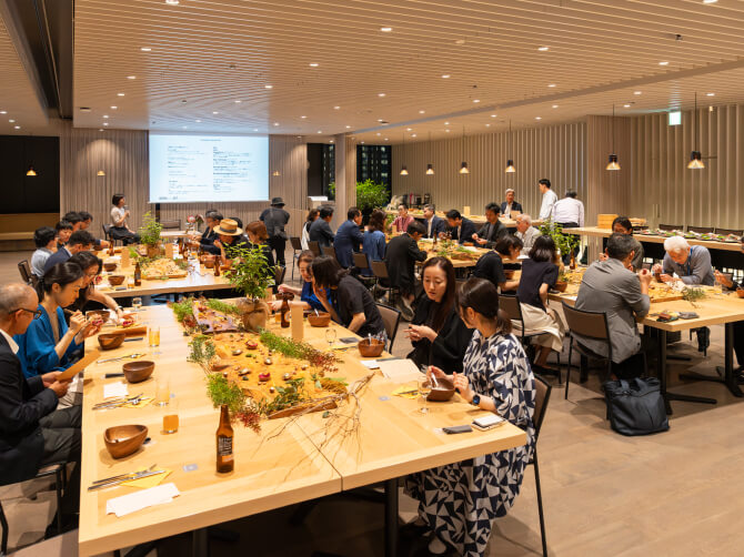 大きなテーブルを囲んで参加者が食事を楽しみながら談笑するフードイベント会場の全景。