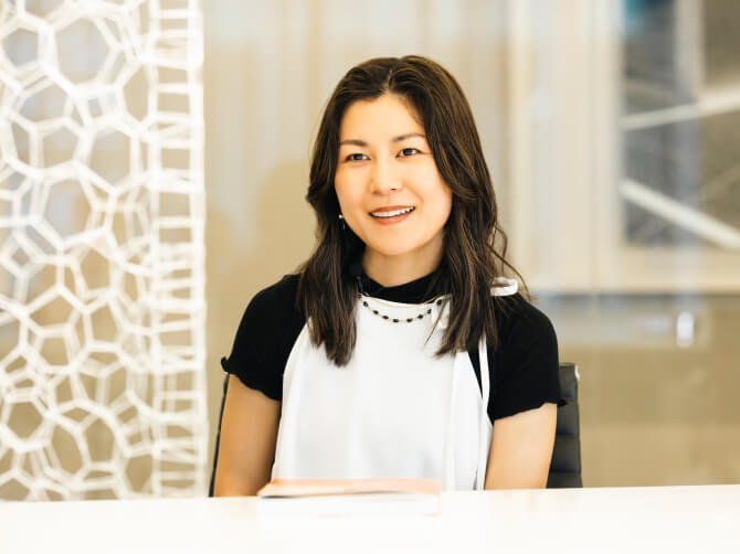 椅子に座り、微笑みながら話す上田杏菜氏。テーブルの上には冊子が置かれている。