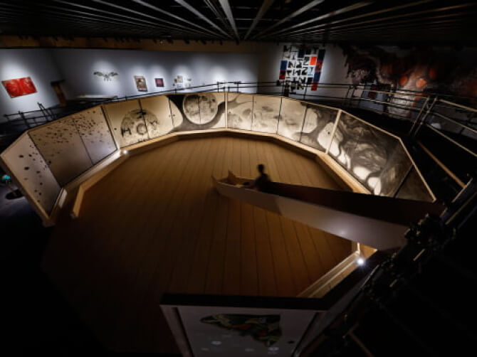 円形の展示空間を俯瞰した写真。壁面に大きなモノクロの作品が並び、中央の空間に向かってスロープが伸びている。薄暗い照明の中、作品が強調されている。
