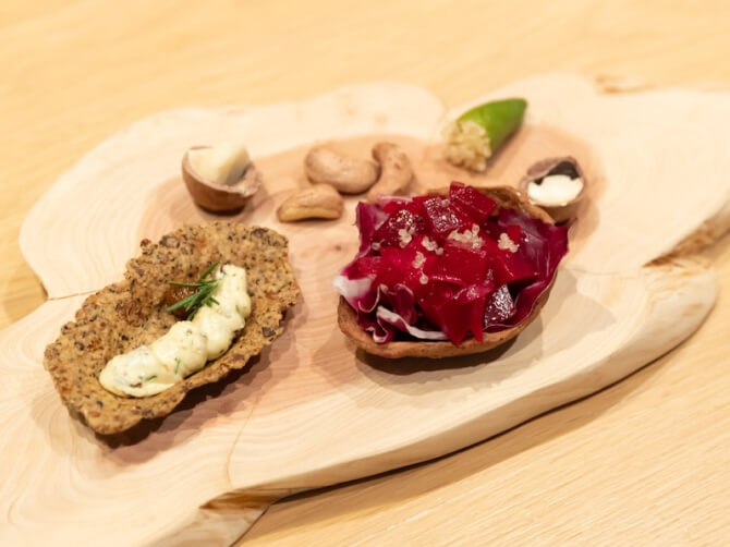 木のプレートに盛り付けられた料理のクローズアップ。赤い野菜を使った料理やディップが添えられたクラッカーなど、色鮮やかな食材が並ぶ。