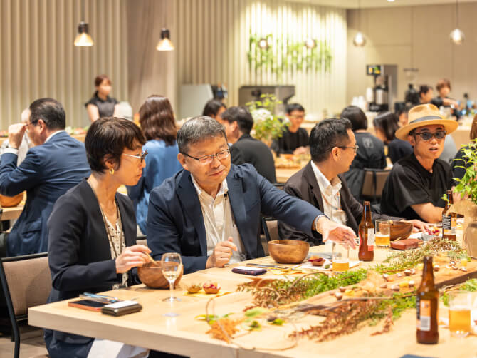 参加者たちが同じテーブルを囲み、料理を味わいながら会話を楽しむ様子。
