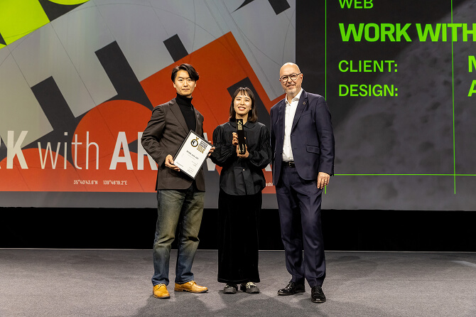 German Design Award 2026 の授賞式で、WORK with ART の受賞者が賞状とトロフィーを手に登壇する様子。