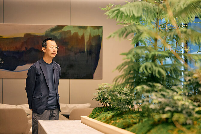 ミュージアムタワー京橋の3階オフィスラウンジにて、穏やかな光と植栽が調和する空間に佇む山口周氏。