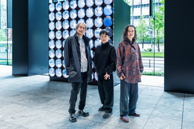 ミュージアムタワー京橋1階のエントランスに設置された《WINDOWS》の前で、左から高谷史郎氏、濱哲史氏、古舘健氏が真剣な表情で並んで立つ写真。