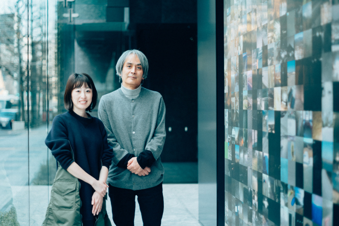 ミュージアムタワー京橋のエントランスにある作品の前に、笑顔の高根枝里氏(左)と落ち着いた表情の高谷史郎氏(右)が並んで立つ写真。高谷史郎氏のインタビュー記事「地球の姿を映したパブリックアート」のサムネイル。