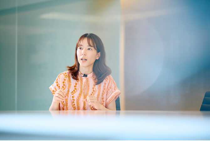 オレンジ色の柄のブラウスを着て話すアーティゾン美術館学芸員の杉本渚氏。「エットレ・ソットサスにフォーカスした、アーティゾン美術館で初となる『デザイン展』」のサムネイル。