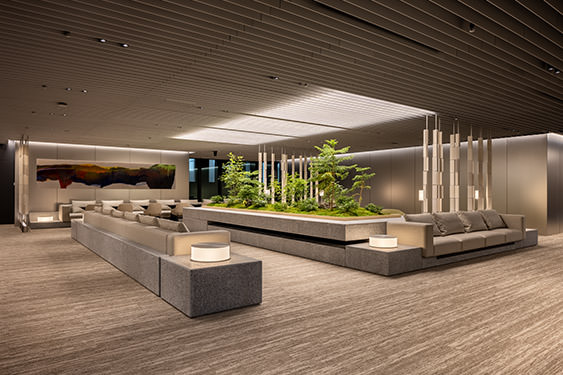 Panoramic view of the office lounge with integrated paintings, plantings, and lighting. The spatial composition is like a salon open to the city.